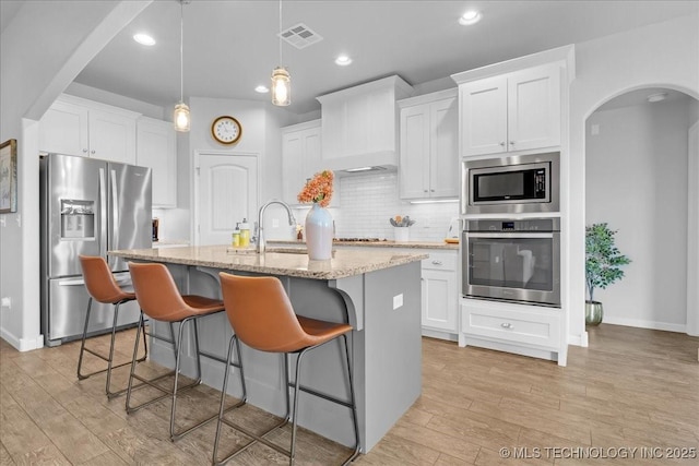 30130 S Maxine Ave, Inola, OK 74036 - kitchen featuring stainless steel appliances, light wood-style flooring, arched walkways, decorative backsplash, and a kitchen island with sink
