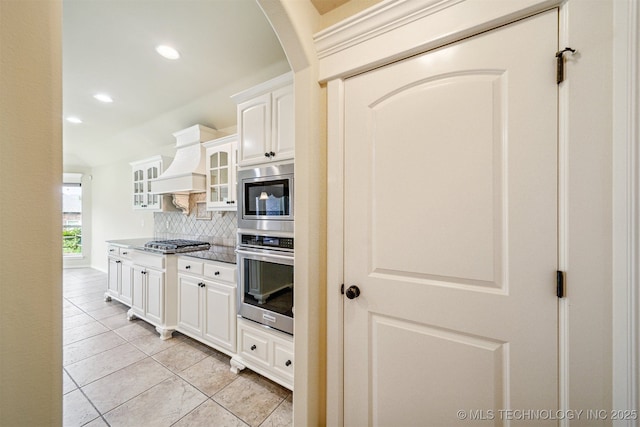 4204 N Maple Pl, Broken Arrow, OK 74012 - kitchen with stainless steel appliances, custom range hood, tasteful backsplash, light tile patterned flooring, and glass insert cabinets