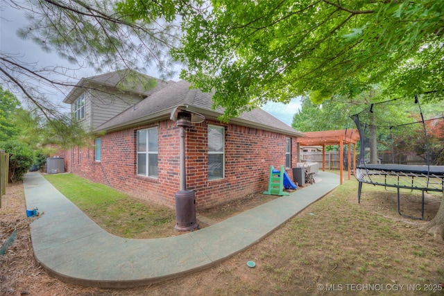 7349 E 119th Pl S, Bixby, OK 74008 - view of side of home with a trampoline, brick siding, a fenced backyard, and roof with shingles