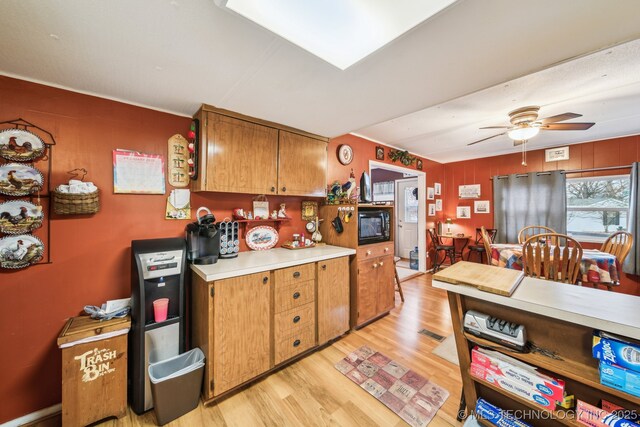 2219 Hart Cove Dr, Grove, OK 74344 - kitchen featuring light wood-type flooring, a ceiling fan, light countertops, black microwave, and brown cabinetry