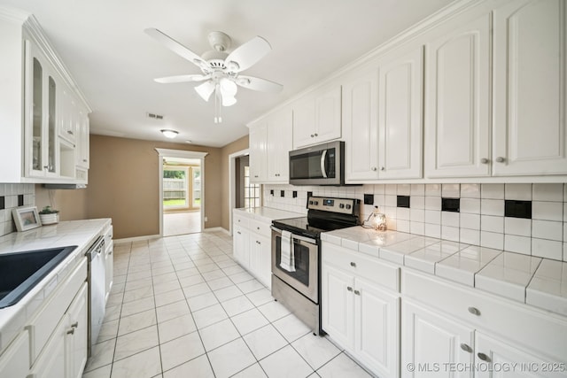 106 E 21st St, Owasso, OK 74055 - kitchen featuring appliances with stainless steel finishes, tile countertops, ceiling fan, and tasteful backsplash