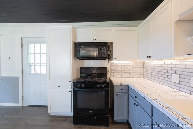 604 N N W, Konawa, OK 74849 - kitchen featuring black appliances, tile countertops, white cabinets, tasteful backsplash, and wood finished floors