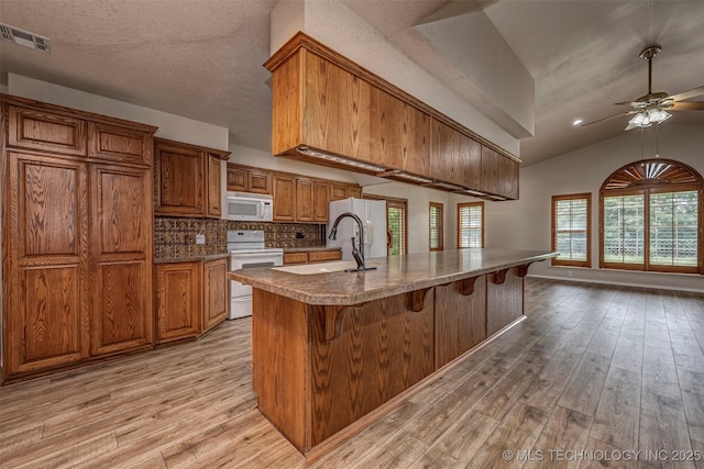 710 N Brethren Rd, Cushing, OK 74023 - kitchen featuring white appliances, brown cabinetry, light wood-style flooring, ceiling fan, and a breakfast bar