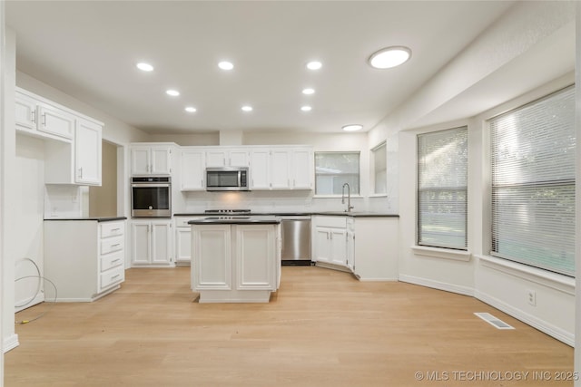 6905 S Redbud Ave, Broken Arrow, OK 74011 - kitchen with dark countertops, light wood-type flooring, white cabinets, a kitchen island, and recessed lighting