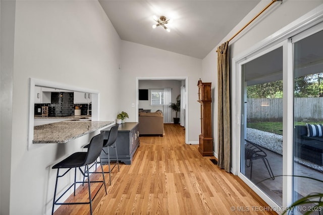 4620 S Winston Ave, Tulsa, OK 74135 - kitchen with light wood-type flooring, a kitchen bar, light stone counters, decorative backsplash, and high vaulted ceiling