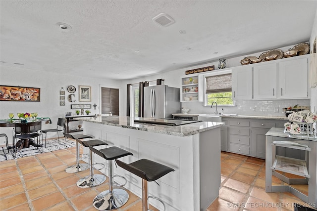 4080 Bud Dr, Sulphur, OK 73086 - kitchen featuring freestanding refrigerator, a textured ceiling, light stone counters, a center island, and a breakfast bar