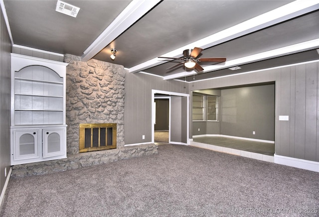 10046 E 29th St, Tulsa, OK 74129 - unfurnished living room featuring ceiling fan, beamed ceiling, carpet flooring, a stone fireplace, and wooden walls