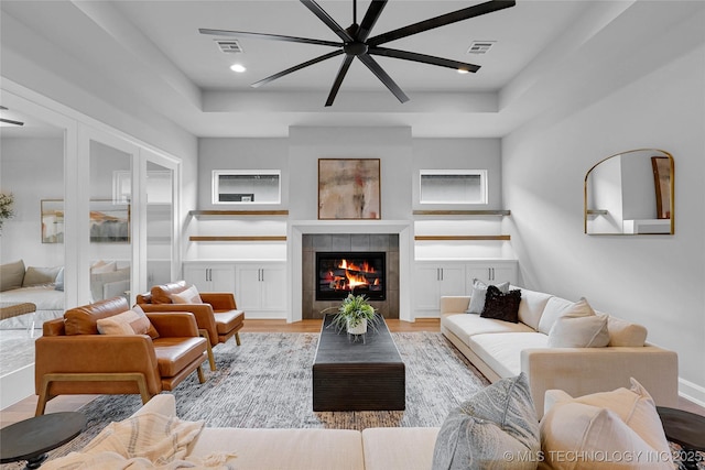 9613 E 119th Ct S, Bixby, OK 74008 - living room featuring a ceiling fan, a tile fireplace, light wood-style flooring, a raised ceiling, and wainscoting