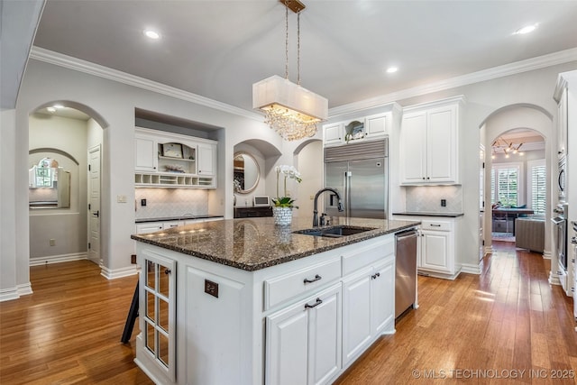 1536 E 35th Pl, Tulsa, OK 74105 - kitchen featuring appliances with stainless steel finishes, arched walkways, a kitchen island with sink, light wood finished floors, and ornamental molding