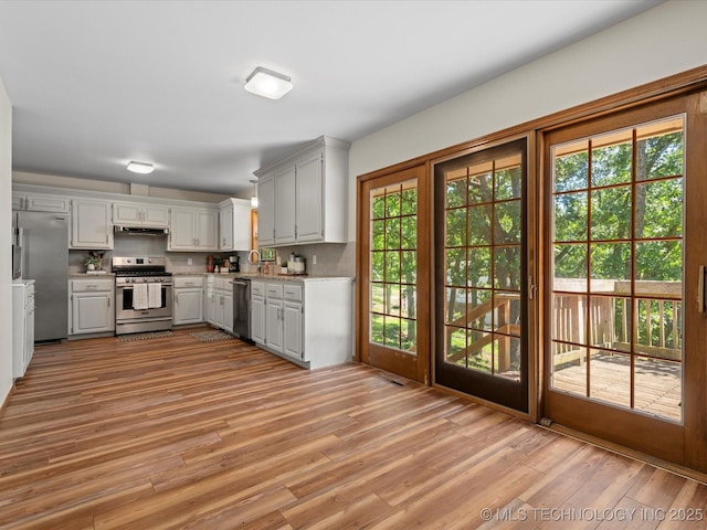 3321 Woodland Rd, Bartlesville, OK 74006 - kitchen featuring appliances with stainless steel finishes, light countertops, light wood-type flooring, tasteful backsplash, and under cabinet range hood