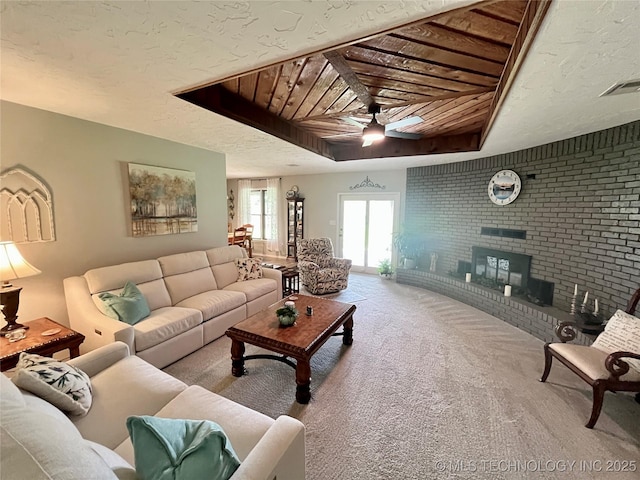 2807 Irving St, Muskogee, OK 74403 - carpeted living room featuring a ceiling fan, a fireplace, a raised ceiling, wood ceiling, and brick wall