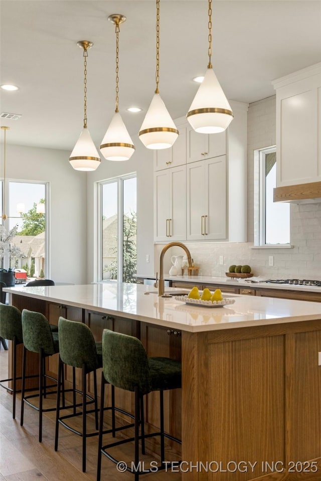7221 E Norman St, Broken Arrow, OK 74014 - kitchen featuring tasteful backsplash, a center island with sink, light wood-type flooring, a breakfast bar, and pendant lighting