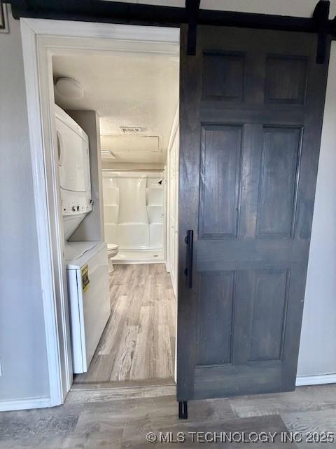 1730 E 67th St Unit K104, Tulsa, OK 74136 - laundry area with stacked washing machine and dryer, a barn door, and light wood finished floors