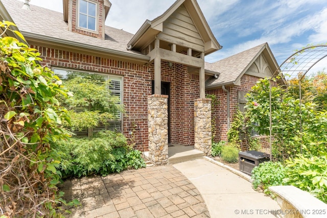 9314 N 96th E Ave, Owasso, OK 74055 - doorway to property featuring brick siding, roof with shingles, and a patio