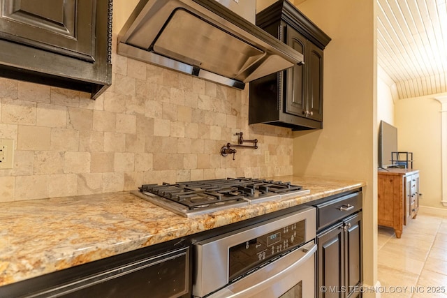 9314 N 96th E Ave, Owasso, OK 74055 - kitchen with premium range hood, stainless steel appliances, decorative backsplash, light stone counters, and dark brown cabinetry