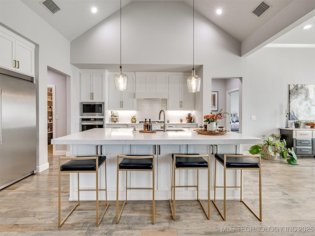 13642 S 21st Pl E, Bixby, OK 74008 - kitchen featuring built in appliances, light countertops, white cabinets, light wood-style floors, and a kitchen bar