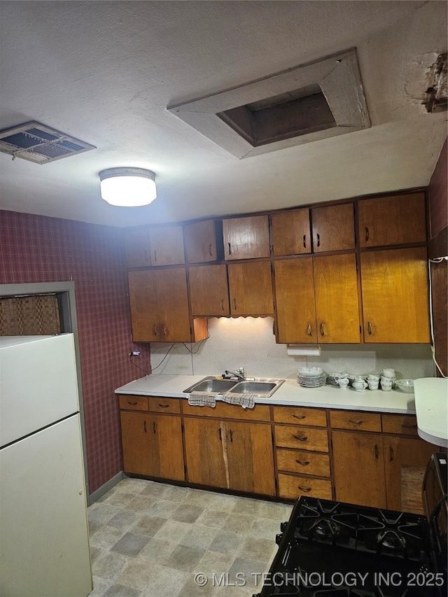 307 N Hartman Ave, Cushing, OK 74023 - kitchen with freestanding refrigerator, brown cabinets, light flooring, light countertops, and wallpapered walls