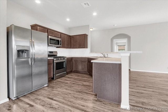 3729 S 150th E Ave, Tulsa, OK 74134 - kitchen featuring appliances with stainless steel finishes, light wood-type flooring, a peninsula, arched walkways, and light countertops