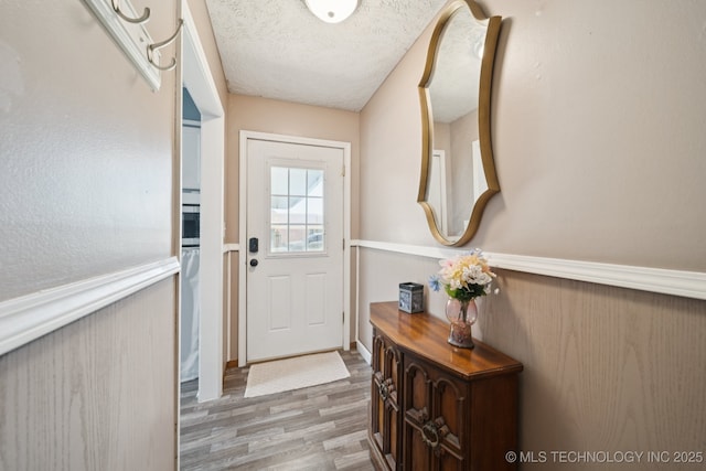 208 N Davis Ave W, Claremore, OK 74017 - doorway to outside featuring wood finished floors, wainscoting, and a textured ceiling