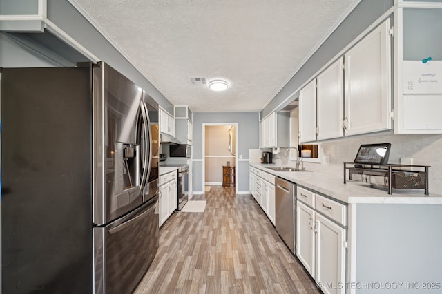 208 N Davis Ave W, Claremore, OK 74017 - kitchen with stainless steel appliances, light countertops, a textured ceiling, light wood-style flooring, and white cabinetry