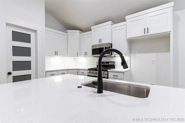 214 S 26th St, Collinsville, OK 74021 - kitchen with appliances with stainless steel finishes, light stone countertops, backsplash, white cabinetry, and vaulted ceiling