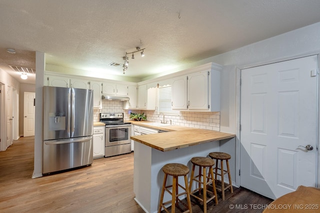 2520 Arlington Blvd, Ada, OK 74820 - kitchen featuring appliances with stainless steel finishes, under cabinet range hood, a peninsula, tasteful backsplash, and light wood-style floors