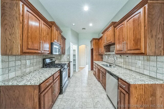 12003 S Tamarack St W, Jenks, OK 74037 - kitchen with stainless steel appliances, arched walkways, light stone counters, brown cabinetry, and tasteful backsplash