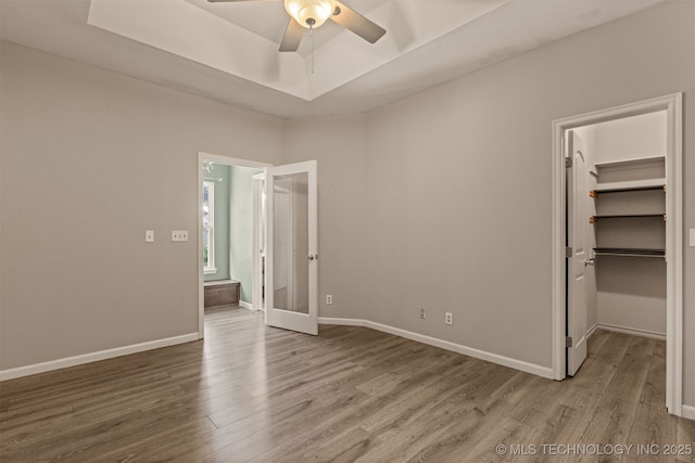 108 W 135th St, Skiatook, OK 74070 - unfurnished bedroom with wood finished floors, a walk in closet, a tray ceiling, a closet, and a ceiling fan