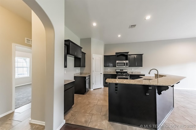 17409 E 44th St S, Tulsa, OK 74134 - kitchen with stainless steel appliances, arched walkways, dark cabinets, a large island with sink, and light stone countertops