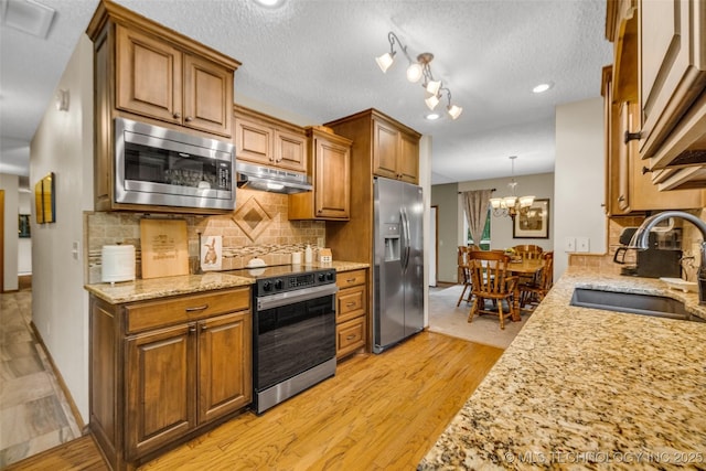 9601 Spring Lake Dr, Broken Arrow, OK 74014 - kitchen featuring stainless steel appliances, under cabinet range hood, light wood-style flooring, brown cabinets, and decorative backsplash