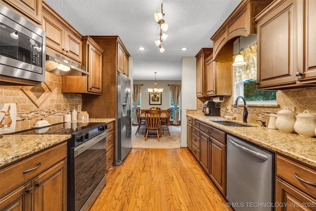 9601 Spring Lake Dr, Broken Arrow, OK 74014 - kitchen with stainless steel appliances, under cabinet range hood, light wood-type flooring, a chandelier, and brown cabinetry