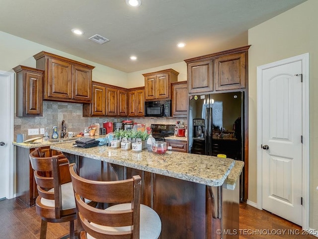 1125 Emily Ln, Ada, OK 74820 - kitchen featuring black appliances, dark wood-type flooring, a center island, tasteful backsplash, and light stone countertops