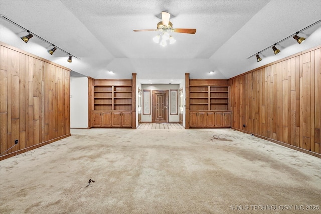 2425 E 53rd St, Tulsa, OK 74105 - unfurnished living room with rail lighting, wood walls, built in features, a textured ceiling, and lofted ceiling