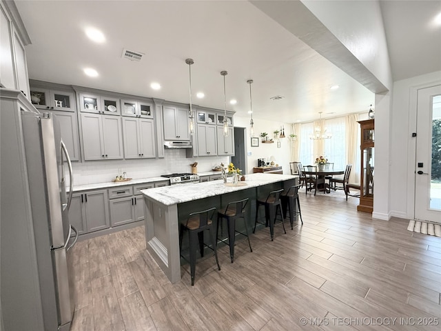 18040 County Road 1558, Ada, OK 74820 - kitchen with stainless steel appliances, gray cabinetry, under cabinet range hood, a kitchen bar, and an island with sink