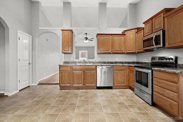 40 E Fairlane Pl, Sapulpa, OK 74066 - kitchen with appliances with stainless steel finishes, ceiling fan, brown cabinetry, a high ceiling, and arched walkways