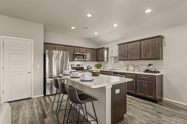7420 E 160th Pl S, Bixby, OK 74008 - kitchen featuring appliances with stainless steel finishes, dark brown cabinetry, dark wood-style floors, a breakfast bar, and a kitchen island