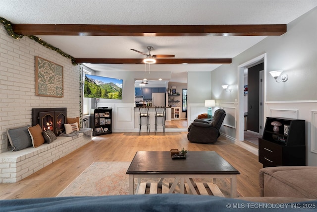 1934 Birnamwood, Miami, OK 74354 - living room featuring wood finished floors, a ceiling fan, a wainscoted wall, a fireplace, and beam ceiling