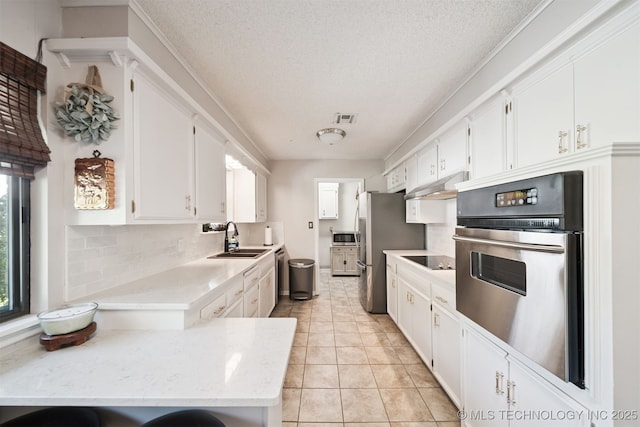 7058 E 52nd Pl, Tulsa, OK 74145 - kitchen featuring stainless steel appliances, under cabinet range hood, white cabinetry, decorative backsplash, and a textured ceiling