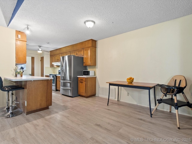 1267 Guinn Ln, Bartlesville, OK 74006 - kitchen with stainless steel appliances, light wood-type flooring, brown cabinets, light countertops, and under cabinet range hood