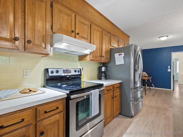 1267 Guinn Ln, Bartlesville, OK 74006 - kitchen featuring stainless steel appliances, under cabinet range hood, brown cabinets, light wood-style floors, and a textured ceiling