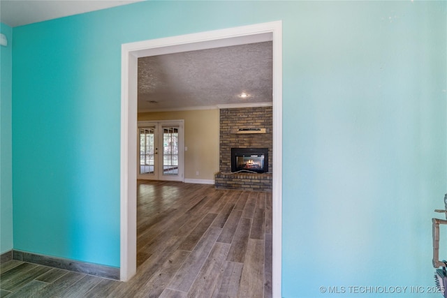 3609 E Scenic Dr, Cushing, OK 74023 - unfurnished living room featuring ornamental molding, wood finished floors, a textured ceiling, a brick fireplace, and french doors