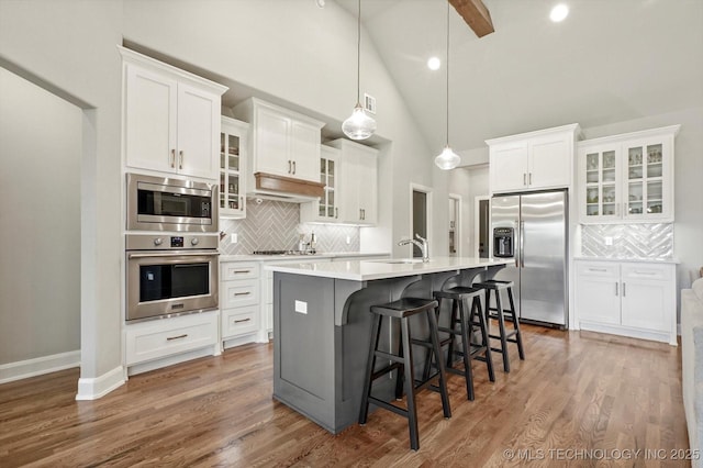 14305 S College Ave, Bixby, OK 74008 - kitchen featuring appliances with stainless steel finishes, decorative backsplash, an island with sink, white cabinets, and high vaulted ceiling