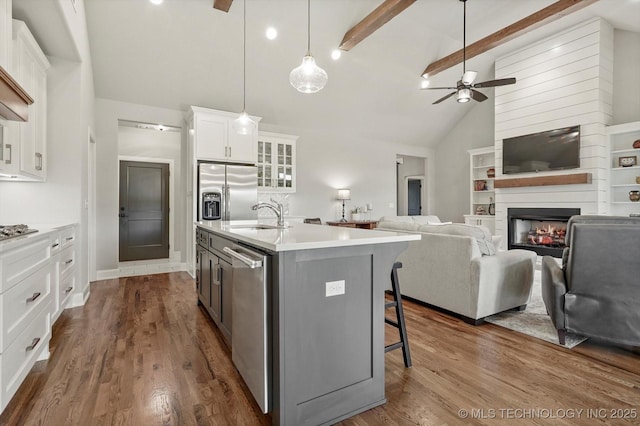 14305 S College Ave, Bixby, OK 74008 - kitchen featuring a ceiling fan, stainless steel appliances, a center island with sink, white cabinetry, and a glass covered fireplace