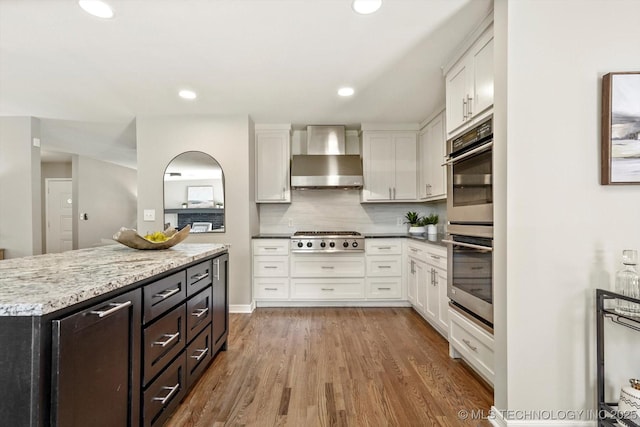 5861 S Hudson Pl, Tulsa, OK 74135 - kitchen featuring wall chimney exhaust hood, appliances with stainless steel finishes, white cabinetry, wood finished floors, and recessed lighting