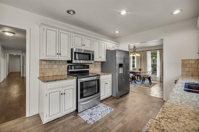 4350 E 74th Pl, Tulsa, OK 74136 - kitchen with stainless steel appliances, wood finished floors, decorative backsplash, white cabinets, and light stone counters
