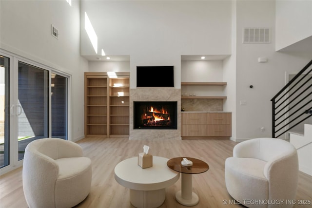 1732 S Jamestown Ave, Tulsa, OK 74112 - living area with light wood-style flooring, a towering ceiling, a lit fireplace, stairs, and built in shelves