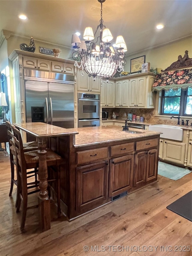 910 Summit Rdg, Mcalester, OK 74501 - kitchen featuring stainless steel appliances, light wood finished floors, a center island with sink, a chandelier, and a breakfast bar area
