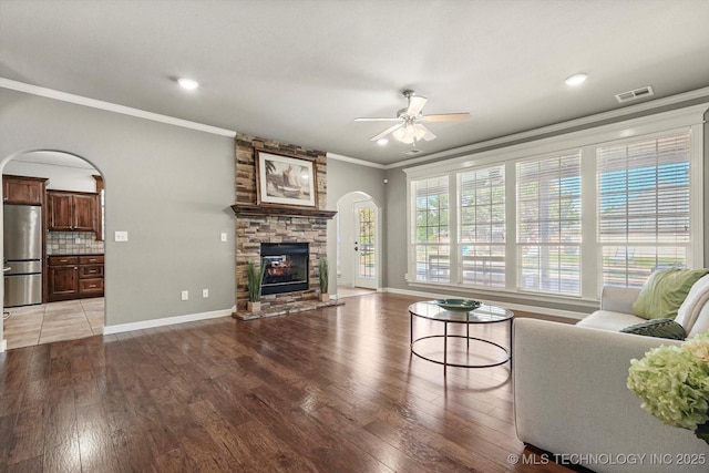 7185 N 194th E Ave, Owasso, OK 74055 - living area featuring arched walkways, crown molding, a ceiling fan, light wood-type flooring, and a stone fireplace