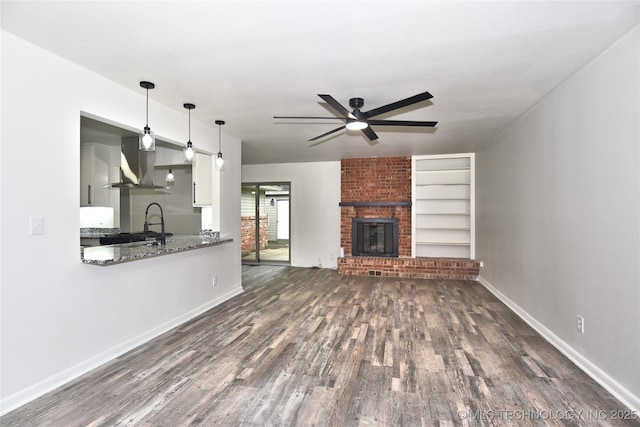5701 S Rockford Pl, Tulsa, OK 74105 - unfurnished living room with a ceiling fan, dark wood-style flooring, a brick fireplace, and built in shelves