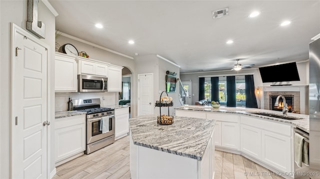 21820 Summit Trl, Claremore, OK 74019 - kitchen featuring appliances with stainless steel finishes, a ceiling fan, a kitchen island, a brick fireplace, and ornamental molding
